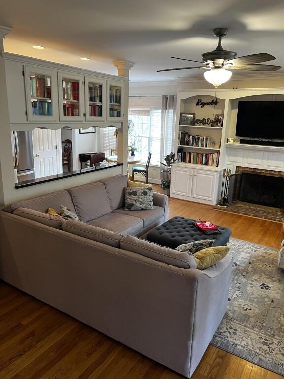 living area featuring ceiling fan, crown molding, a tiled fireplace, and wood finished floors