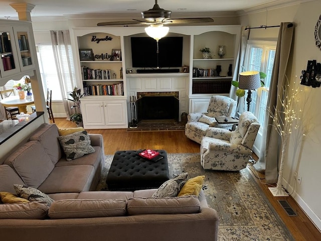 living area featuring ceiling fan, light wood finished floors, a brick fireplace, and crown molding