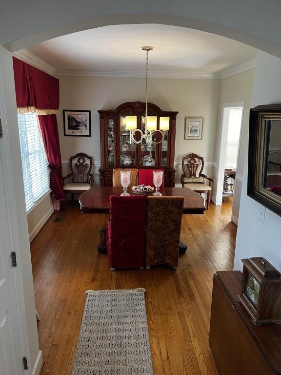 dining area with arched walkways, ornamental molding, wood finished floors, and an inviting chandelier