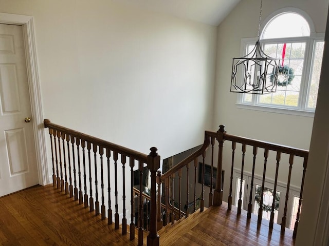 stairs featuring a healthy amount of sunlight, vaulted ceiling, an inviting chandelier, and wood finished floors