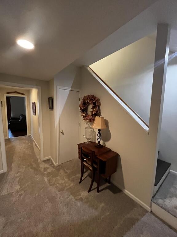 hallway featuring carpet floors, baseboards, and stairs