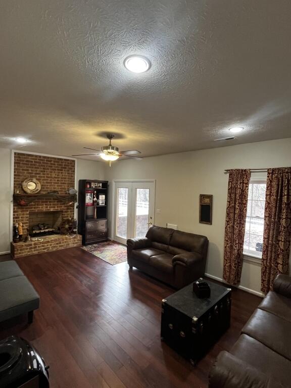 living area with dark wood-style floors, a brick fireplace, a textured ceiling, and a ceiling fan