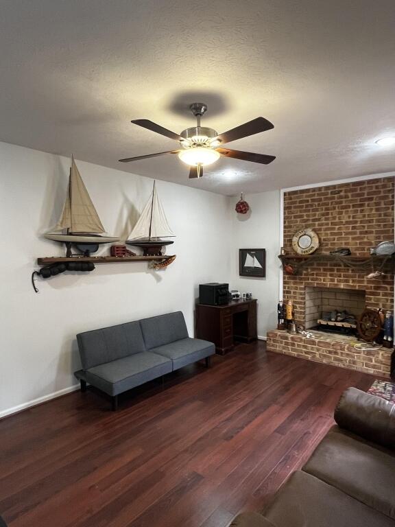 living area with baseboards, ceiling fan, dark wood-type flooring, a textured ceiling, and a brick fireplace