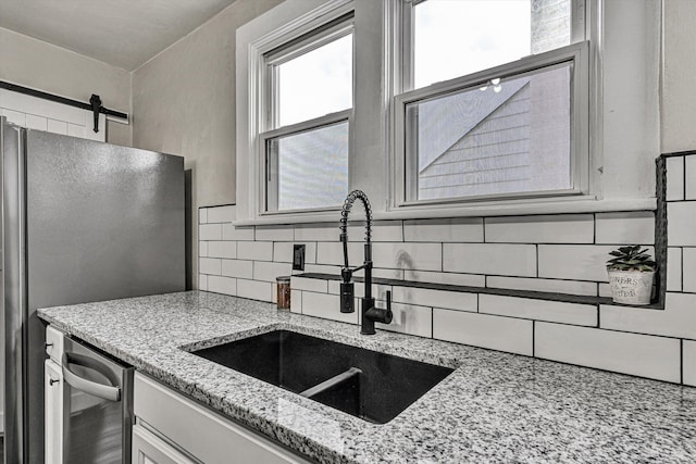 kitchen featuring sink, tasteful backsplash, appliances with stainless steel finishes, a barn door, and light stone countertops