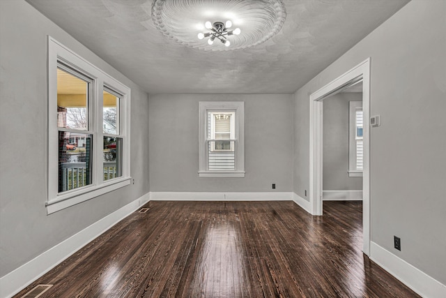 empty room featuring a wealth of natural light, baseboards, dark wood-style flooring, and visible vents