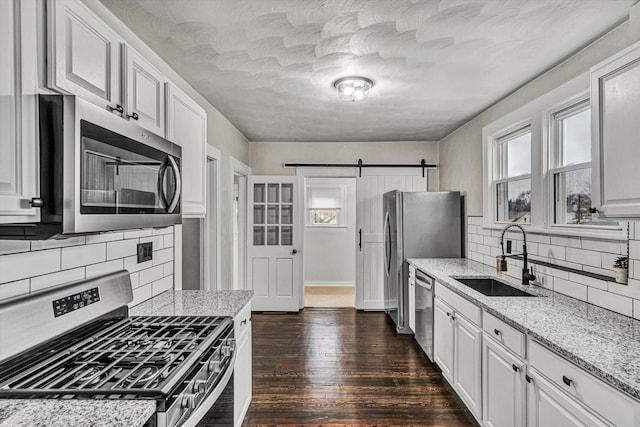 kitchen with sink, light stone counters, stainless steel appliances, a barn door, and white cabinets