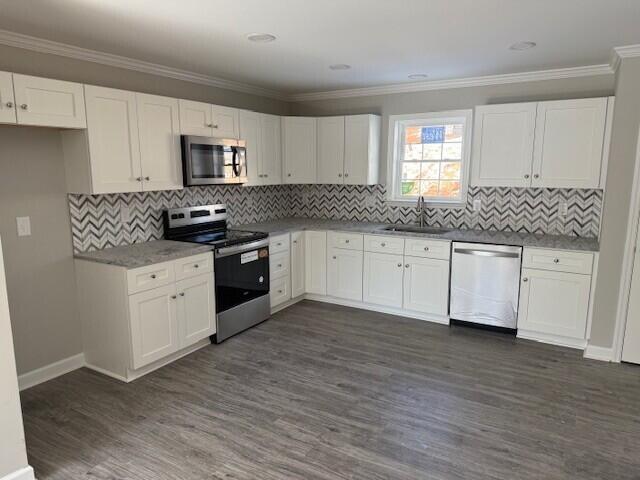 kitchen with dark wood-type flooring, ornamental molding, appliances with stainless steel finishes, white cabinetry, and a sink