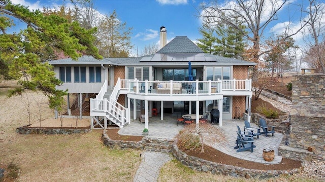 back of house featuring stairs, a patio, and roof mounted solar panels