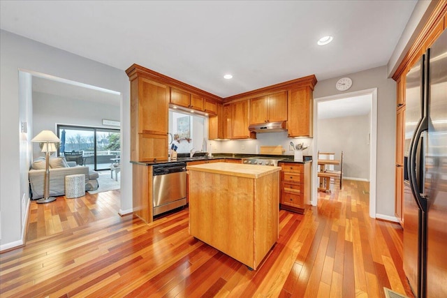 kitchen with wood counters, light wood-type flooring, under cabinet range hood, and stainless steel appliances