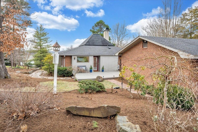 rear view of house featuring a patio area, brick siding, a chimney, and a shingled roof