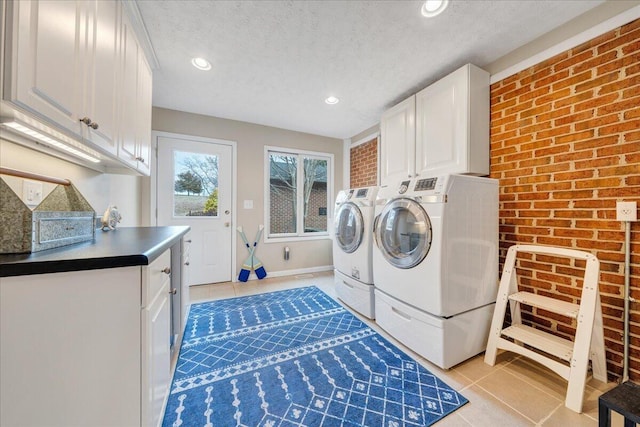 laundry area featuring washer and dryer, a textured ceiling, cabinet space, brick wall, and light tile patterned floors