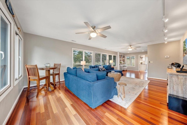 living area with light wood-style flooring, baseboards, ceiling fan, and rail lighting