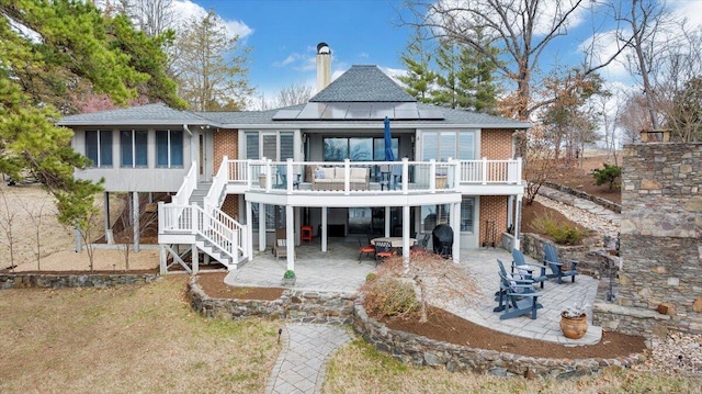 rear view of property with stairs, a patio, brick siding, and roof mounted solar panels