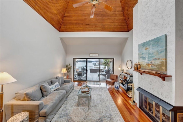 living room featuring high vaulted ceiling, a ceiling fan, wood finished floors, a fireplace, and wood ceiling