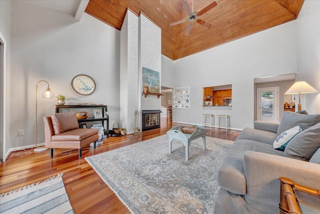 living area featuring wood finished floors, baseboards, a fireplace, ceiling fan, and wood ceiling