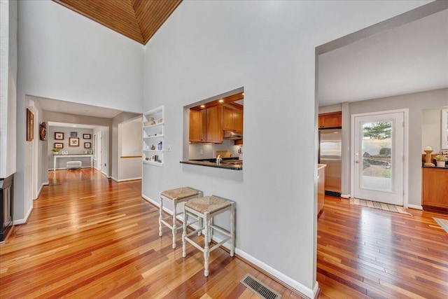 hall with light wood finished floors, visible vents, baseboards, and a towering ceiling