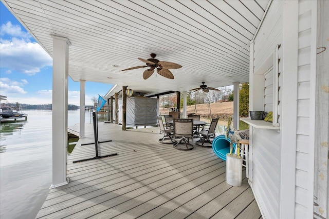 wooden terrace with a water view, ceiling fan, a dock, and outdoor dining space