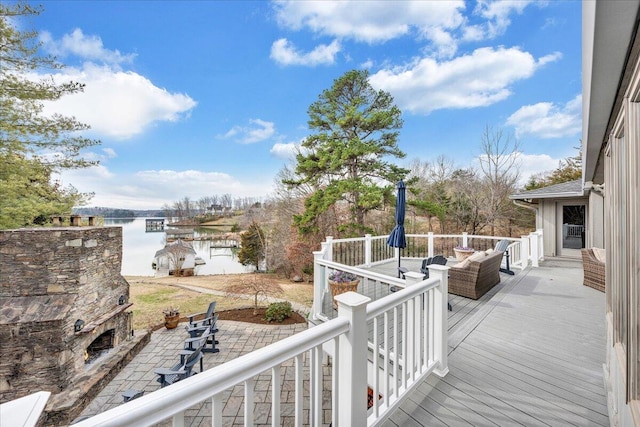 wooden terrace with an outdoor stone fireplace and a water view