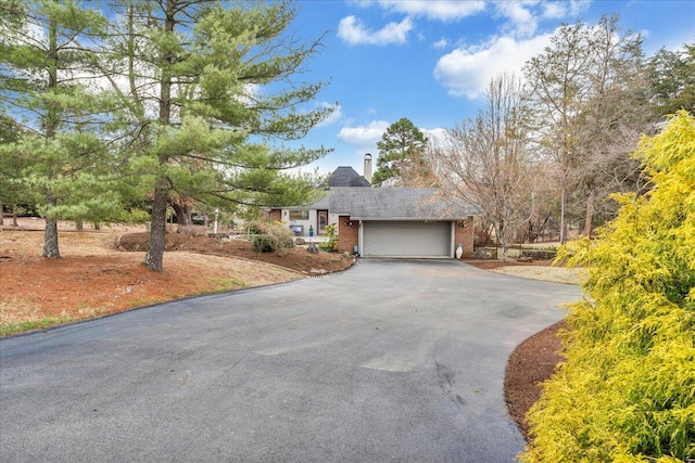 single story home featuring aphalt driveway, a chimney, brick siding, and a garage