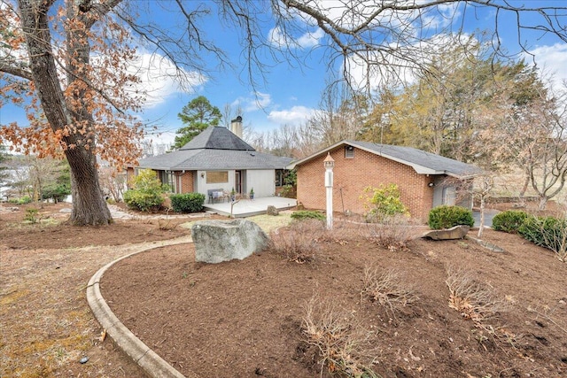 view of front of property featuring a patio, brick siding, and a chimney