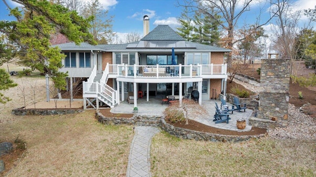 rear view of house featuring brick siding, stairs, roof mounted solar panels, a deck, and a patio