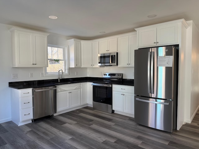 kitchen with appliances with stainless steel finishes, dark countertops, dark wood-style flooring, and white cabinets