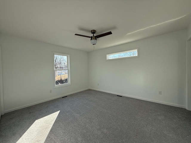 empty room with baseboards, dark colored carpet, visible vents, and a healthy amount of sunlight