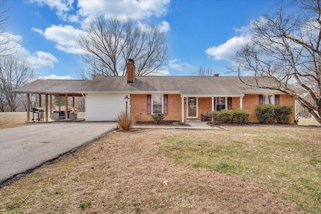 ranch-style home with aphalt driveway, an attached carport, brick siding, a chimney, and a front yard