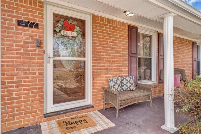 view of exterior entry featuring a porch and brick siding