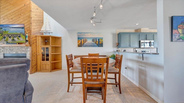 carpeted dining room with rail lighting and a stone fireplace