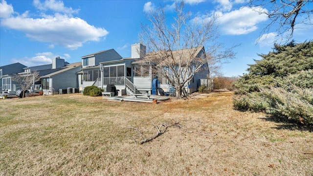 rear view of property featuring central air condition unit, a sunroom, and a lawn