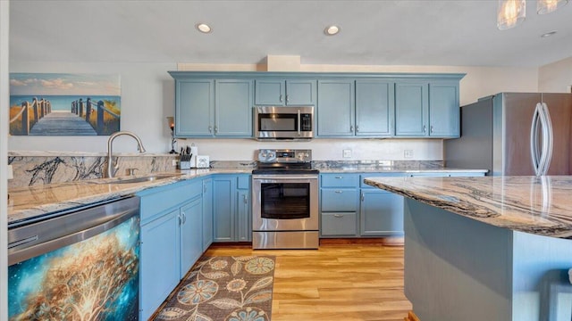 kitchen featuring light wood-type flooring, light stone countertops, blue cabinets, sink, and appliances with stainless steel finishes