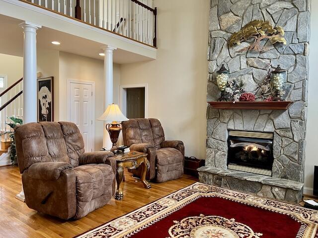 sitting room featuring a towering ceiling, a fireplace, decorative columns, and hardwood / wood-style floors