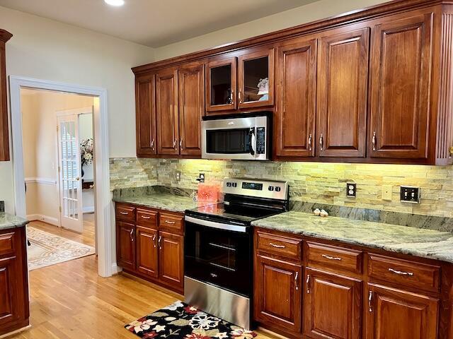 kitchen featuring stainless steel appliances, tasteful backsplash, light stone countertops, and light hardwood / wood-style flooring