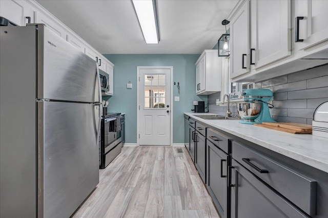 kitchen featuring pendant lighting, sink, white cabinets, stainless steel appliances, and light stone countertops