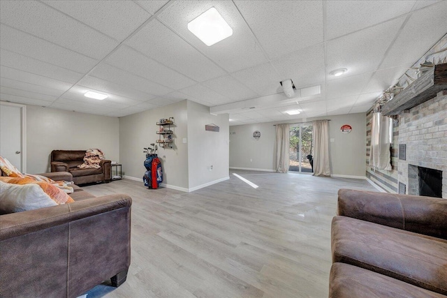 living room featuring a drop ceiling, a brick fireplace, and light hardwood / wood-style flooring