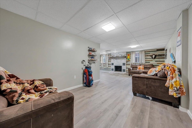 living room featuring a drop ceiling, light hardwood / wood-style flooring, and a large fireplace