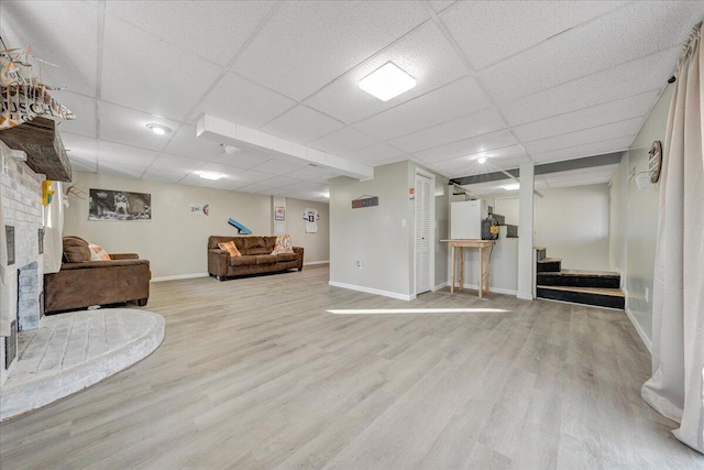 living room with a brick fireplace, a paneled ceiling, and light wood-type flooring