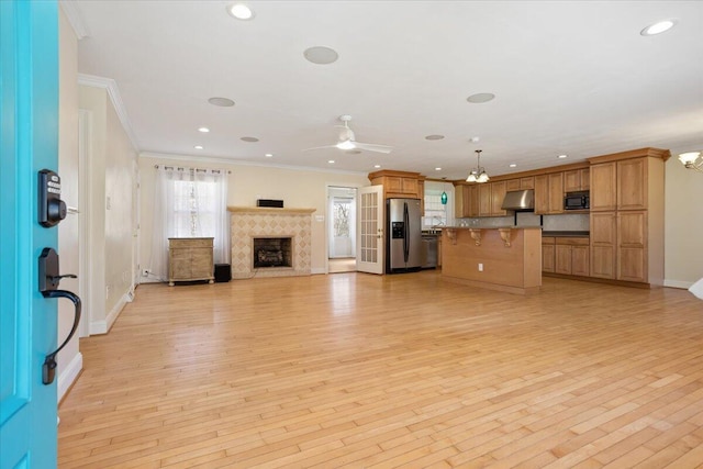 unfurnished living room featuring light wood-type flooring, ornamental molding, a ceiling fan, and a tile fireplace