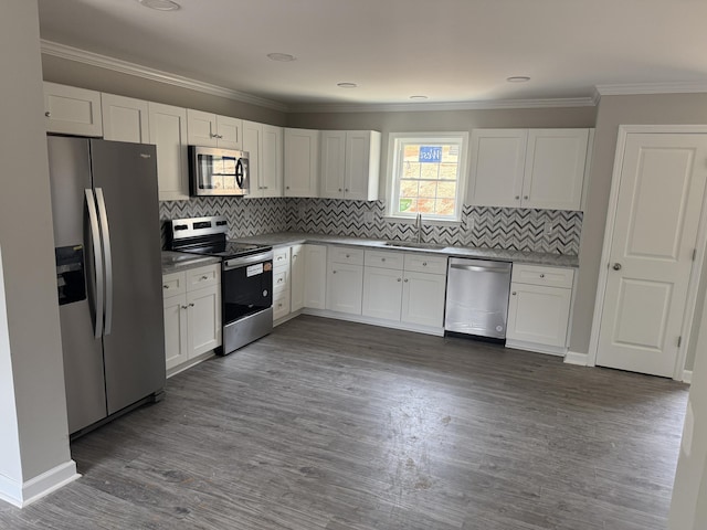 kitchen featuring dark wood-type flooring, ornamental molding, a sink, stainless steel appliances, and white cabinets