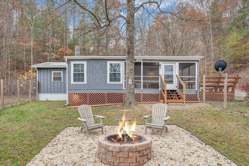 back of property with a sunroom, a lawn, and a fire pit