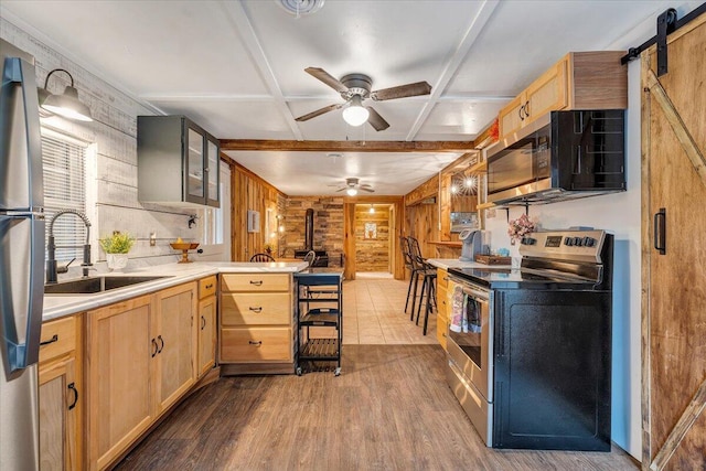 kitchen featuring sink, a wood stove, coffered ceiling, stainless steel appliances, and a barn door