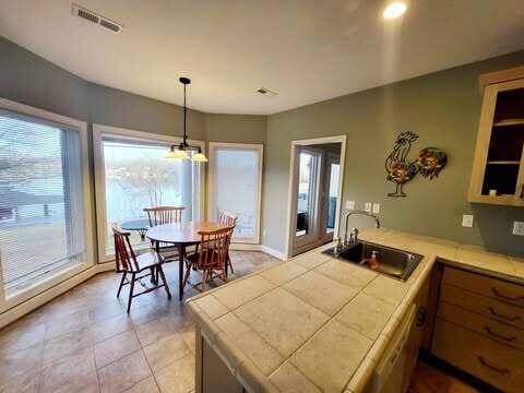 kitchen with light tile patterned flooring, sink, tile countertops, hanging light fixtures, and kitchen peninsula