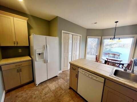 kitchen with sink, white appliances, hanging light fixtures, tile countertops, and light brown cabinets