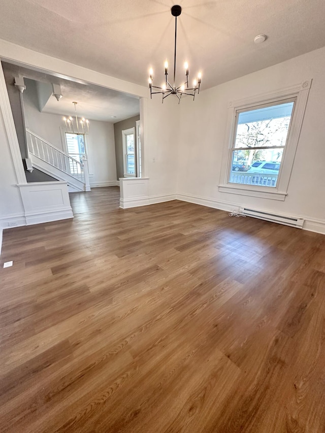 unfurnished dining area with a chandelier, a baseboard heating unit, wood finished floors, and a healthy amount of sunlight