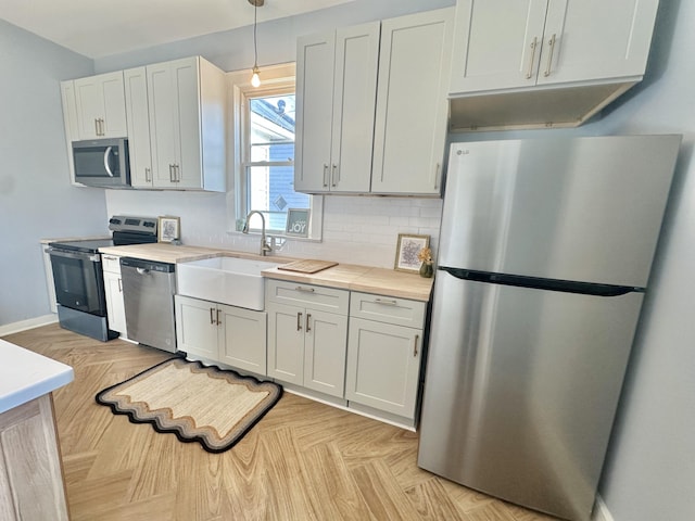 kitchen featuring light countertops, hanging light fixtures, appliances with stainless steel finishes, white cabinetry, and a sink