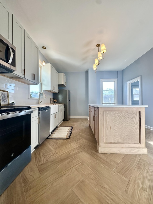 kitchen with white cabinets, a kitchen island, appliances with stainless steel finishes, decorative light fixtures, and light countertops