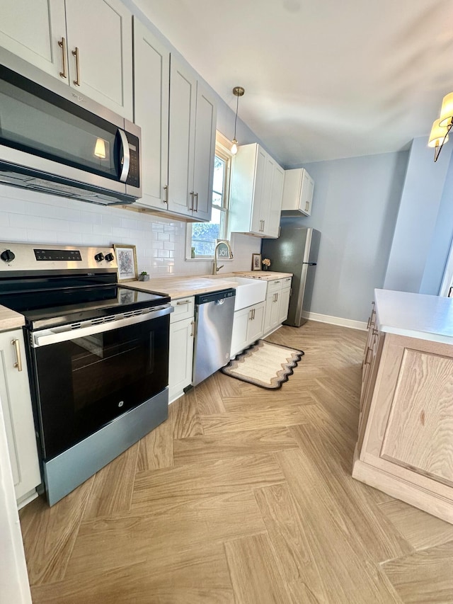 kitchen with stainless steel appliances, white cabinets, hanging light fixtures, light countertops, and tasteful backsplash