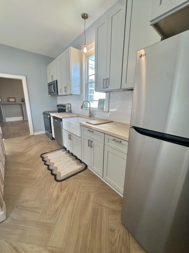 kitchen with pendant lighting, tasteful backsplash, appliances with stainless steel finishes, a sink, and butcher block countertops