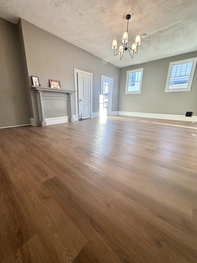 unfurnished dining area with a notable chandelier, a textured ceiling, baseboards, and wood finished floors